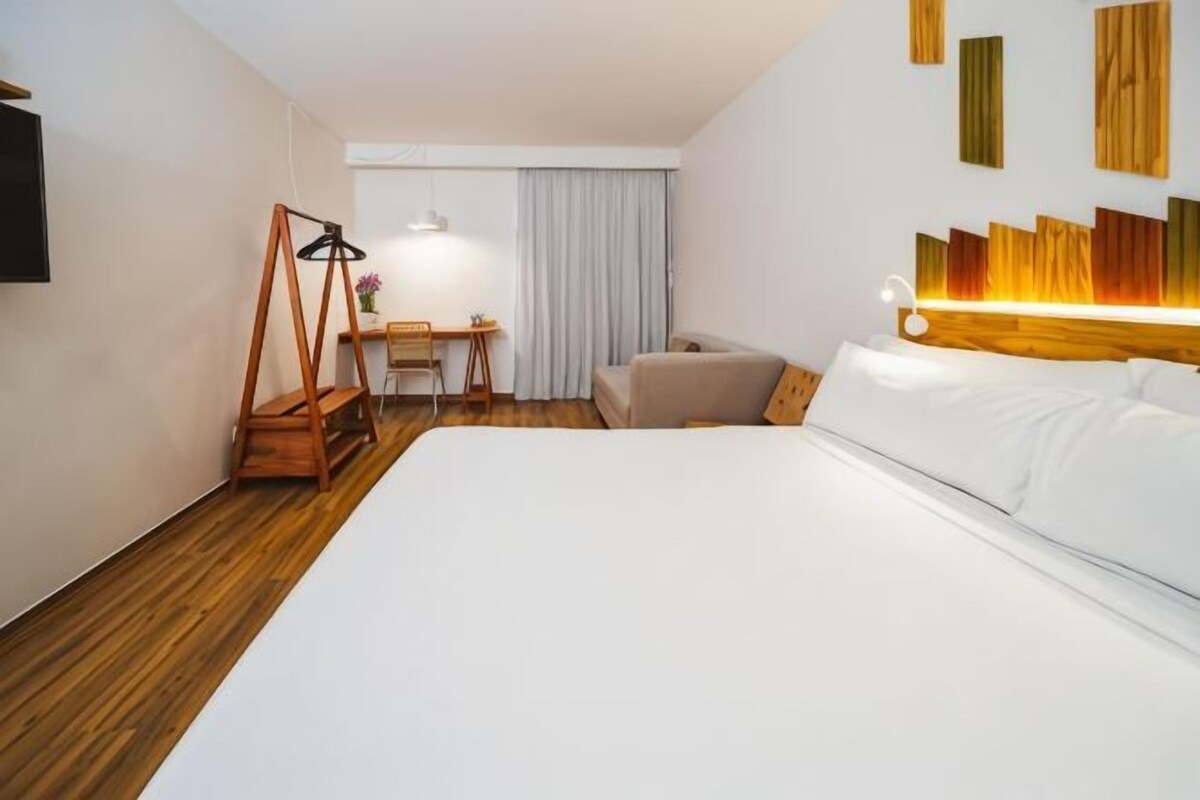 A hotel room with a large bed, a desk, a chair, and a television.