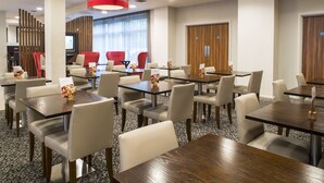 A hotel dining area with multiple tables and chairs, a television, and a red accent wall. - Holiday Inn Express Leicester - City by IHG (Leicester)