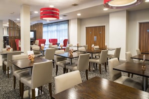 A hotel dining area with multiple tables and chairs, a television, and a red accent wall. - Holiday Inn Express Leicester - City by IHG (Leicester)