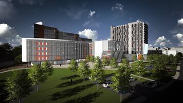 A modern building complex with multiple floors, large windows, and a central courtyard with trees and parked cars.