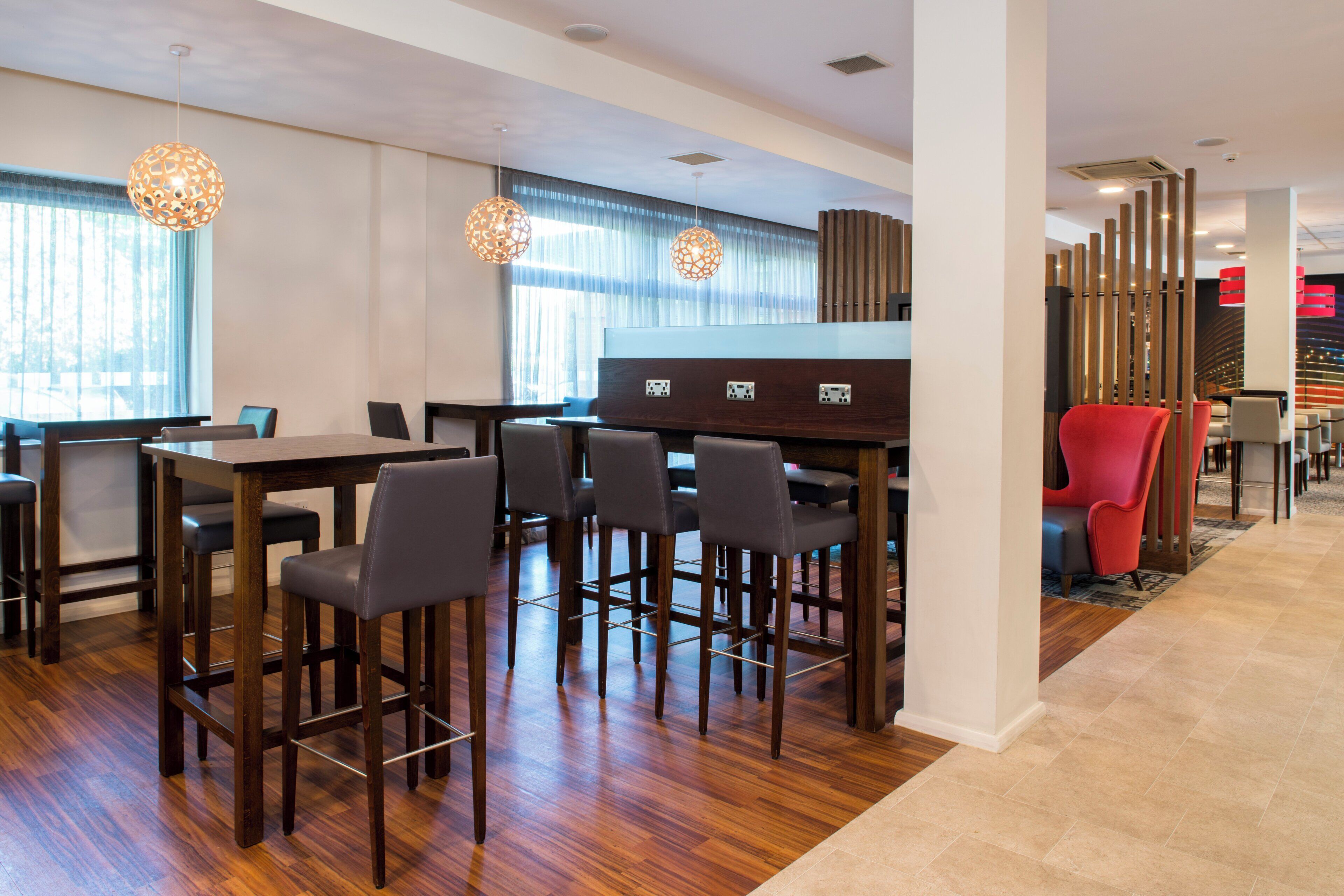 A modern hotel lobby with a bar area, wooden flooring, and pendant lighting.