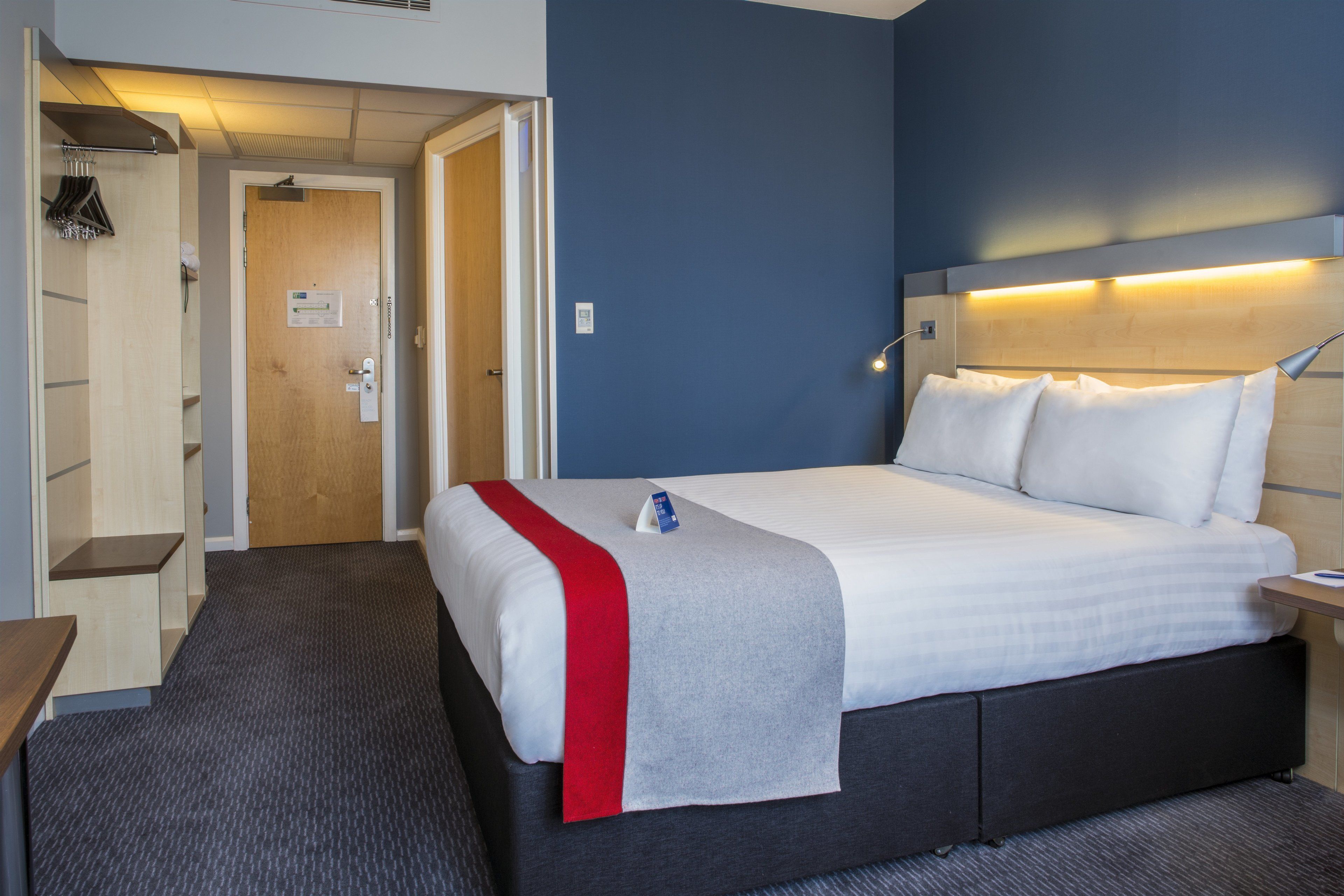 Una camera d'albergo con un letto, un comodino, una scrivania, una sedia, un armadio e una porta.