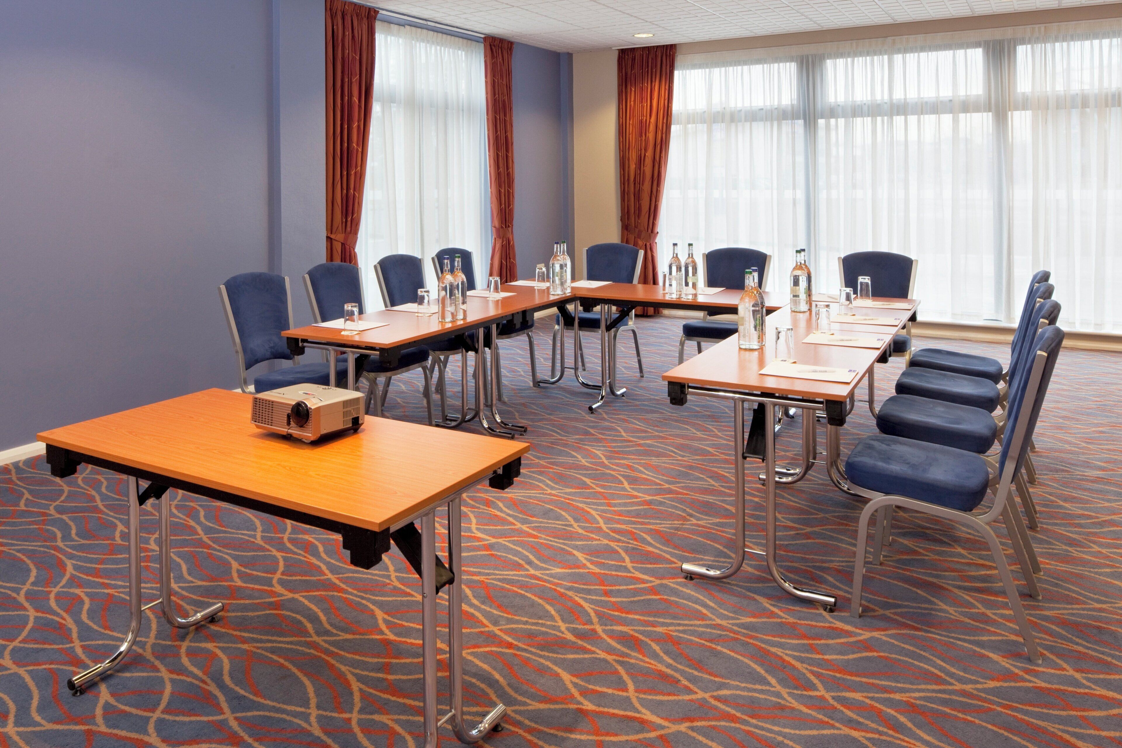 A conference room with a long table, chairs, a projector, and a carpeted floor.