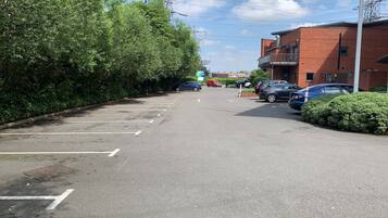 Um estacionamento com vários carros, um edifício de tijolos e uma sebe.