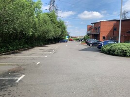 A parking lot with multiple cars, a brick building, and a hedge.