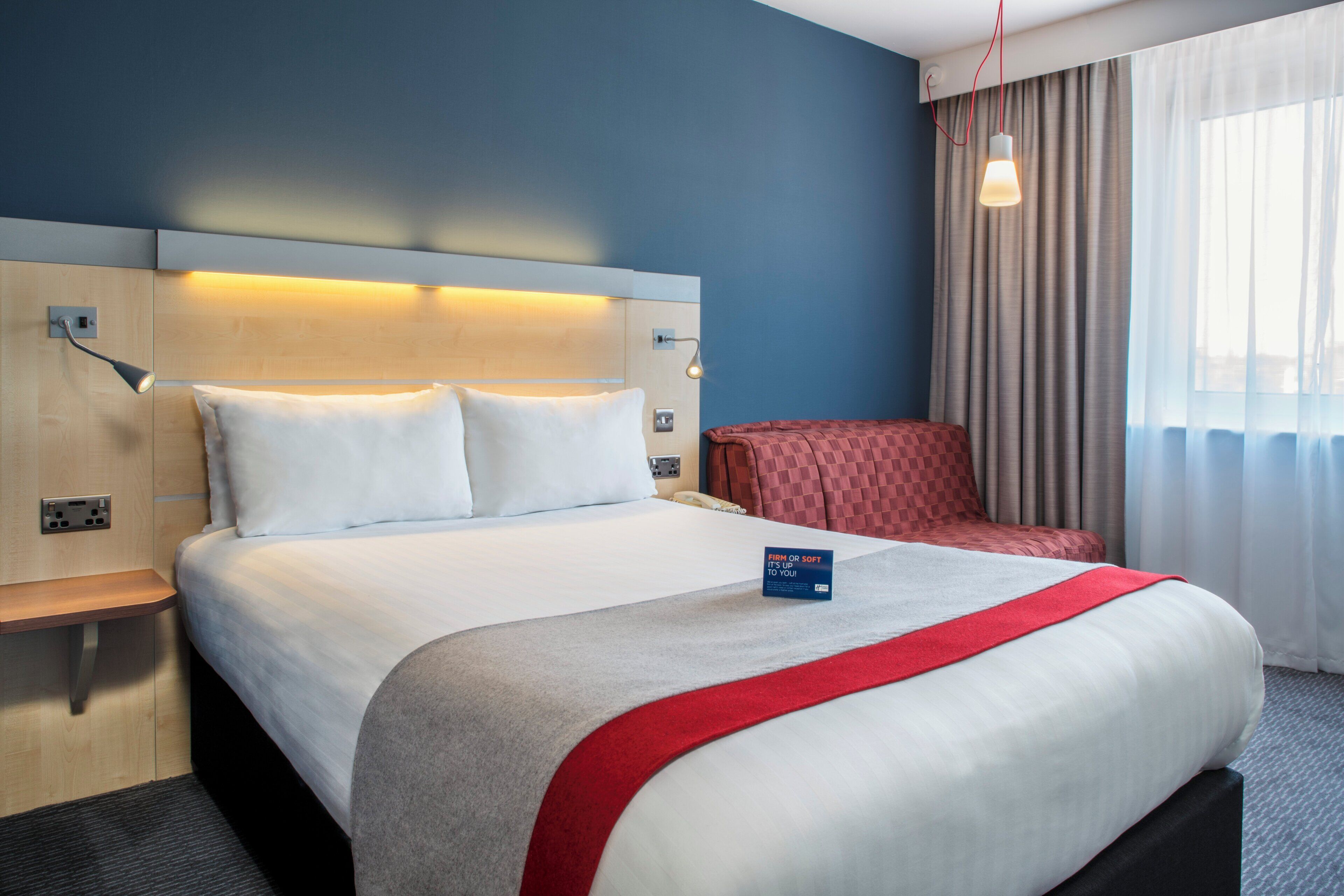 A hotel room with a large bed, a desk, a chair, and a window with curtains.
