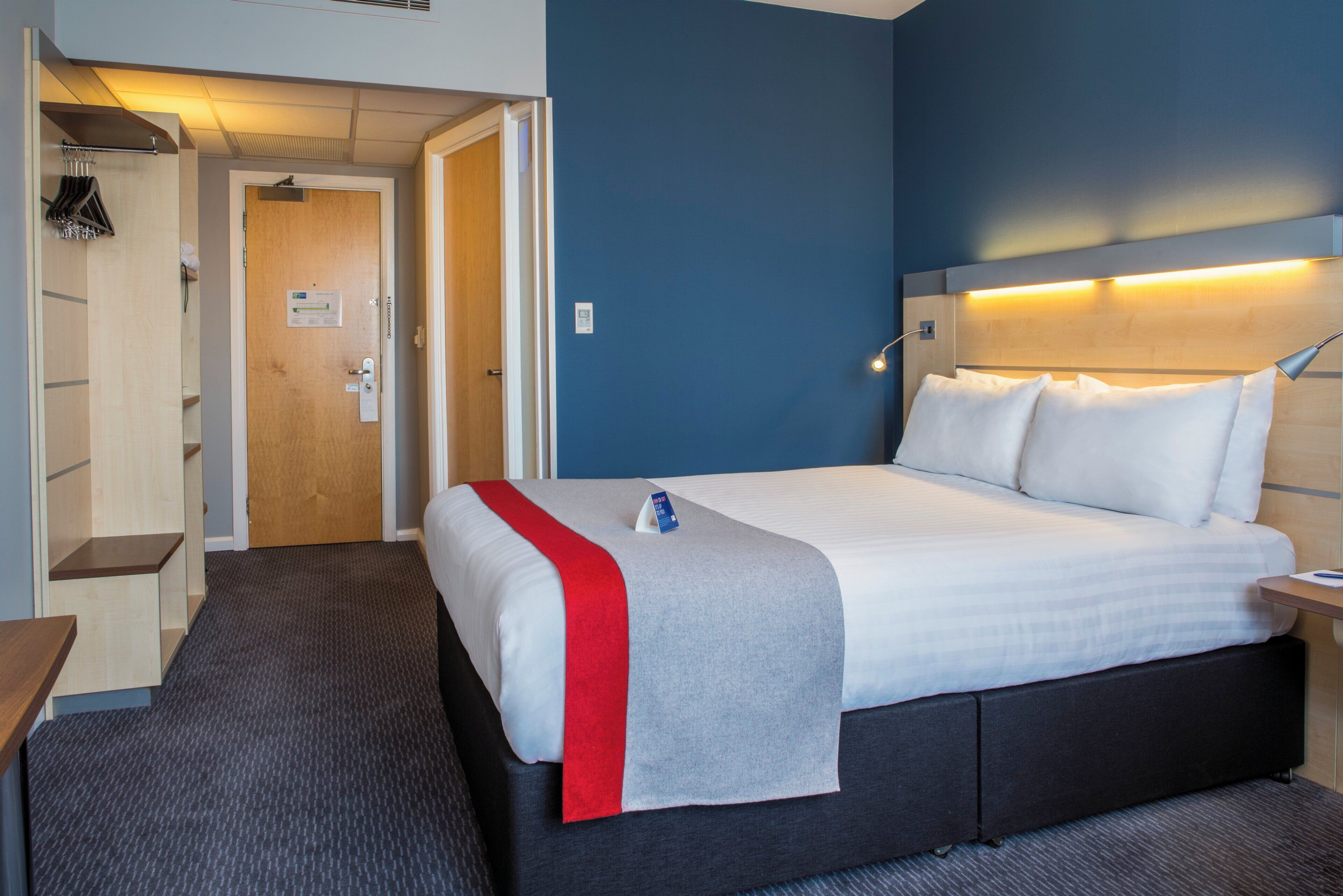 Habitación de hotel con cama, mesita de noche, escritorio, armario y puerta que da a un baño.