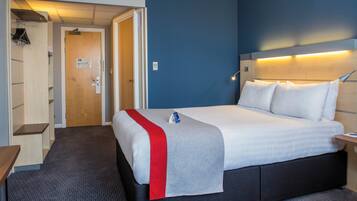 Habitación de hotel con cama, mesita de noche, escritorio, armario y puerta que da a un baño.