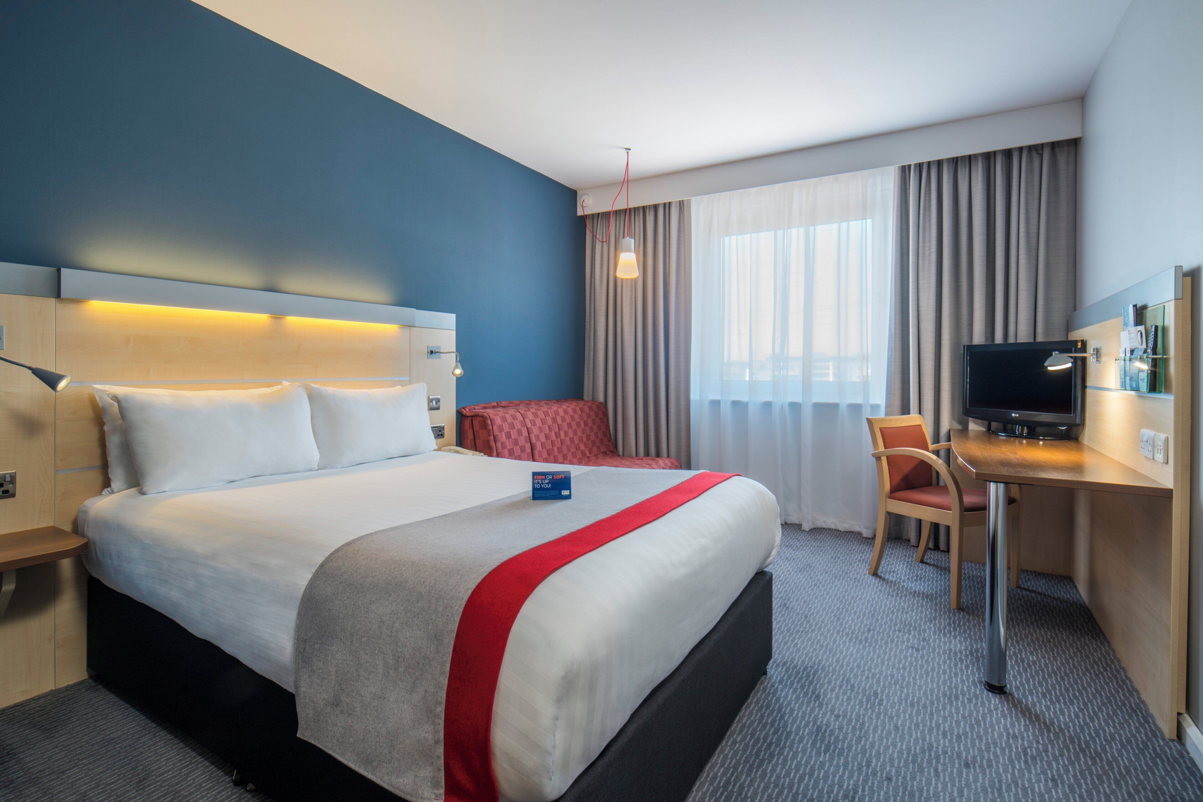 Une chambre d’hôtel avec un grand lit, un bureau avec une télévision, une chaise et une fenêtre avec des rideaux.