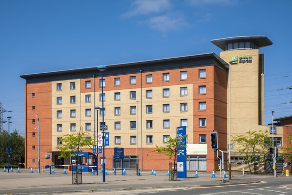 A multi-story hotel with a prominent Holiday Inn Express sign, a parking lot with blue cones, and a clear blue sky. - Holiday Inn Express Leicester - City by IHG (Leicester)