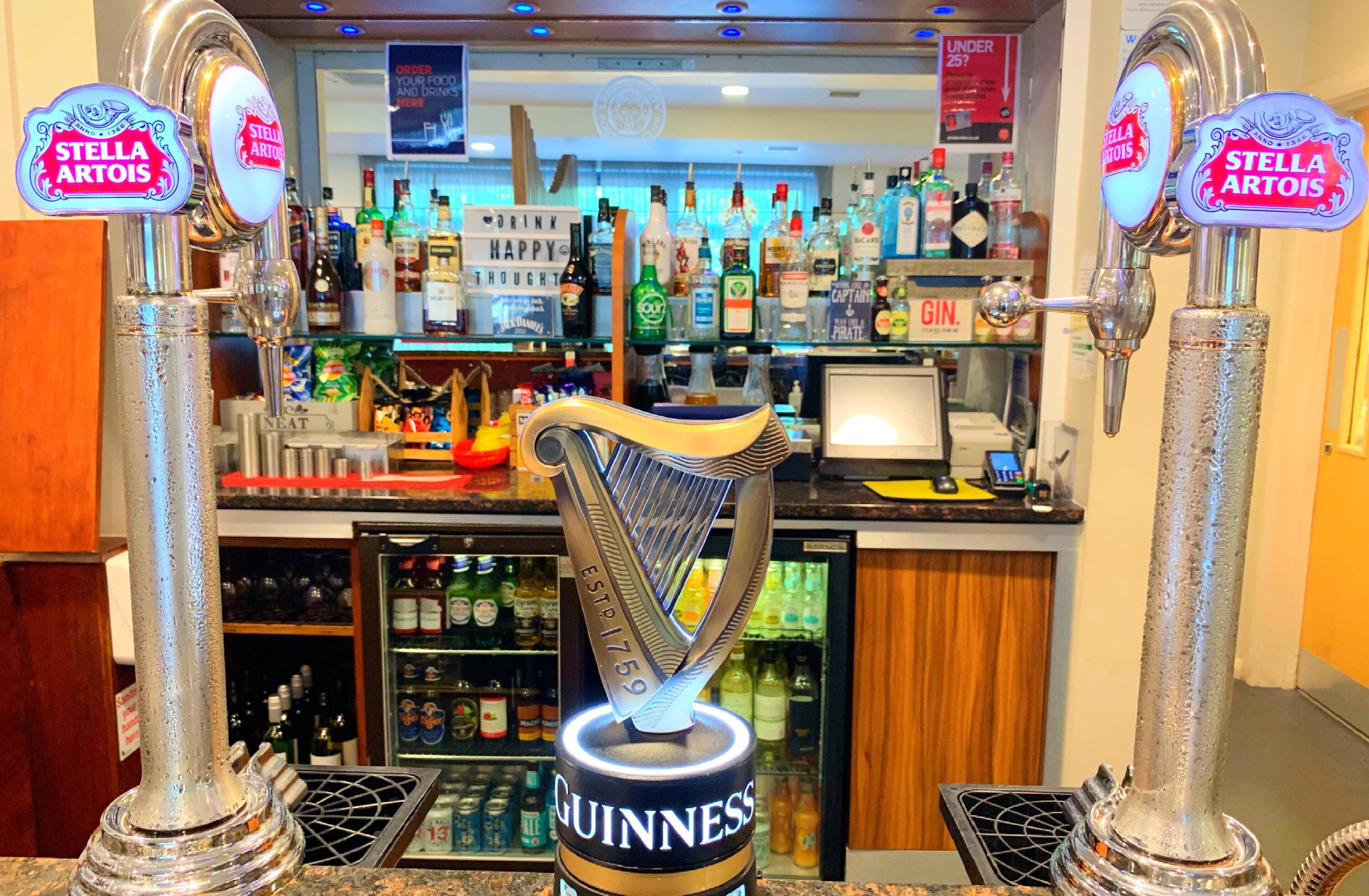 A bar area with multiple beer taps, including brands like Stella Artois and Guinness, and a variety of bottles and glasses on shelves.