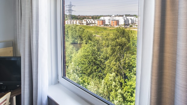 A room with a large window overlooking a green area with trees and buildings in the distance. - Holiday Inn Express Leicester - City by IHG (Leicester)