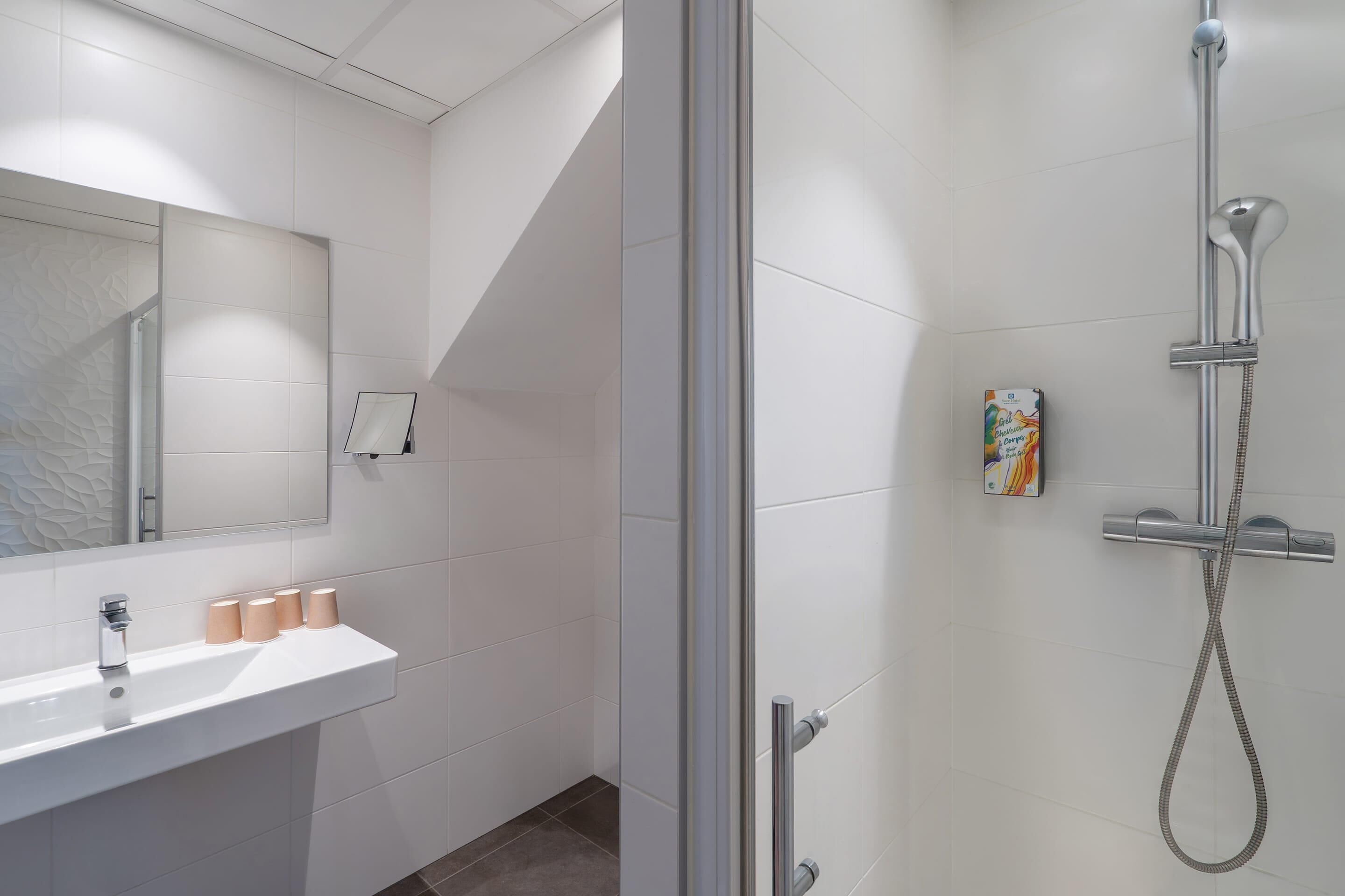 A bathroom with a white sink, mirror, and shower.