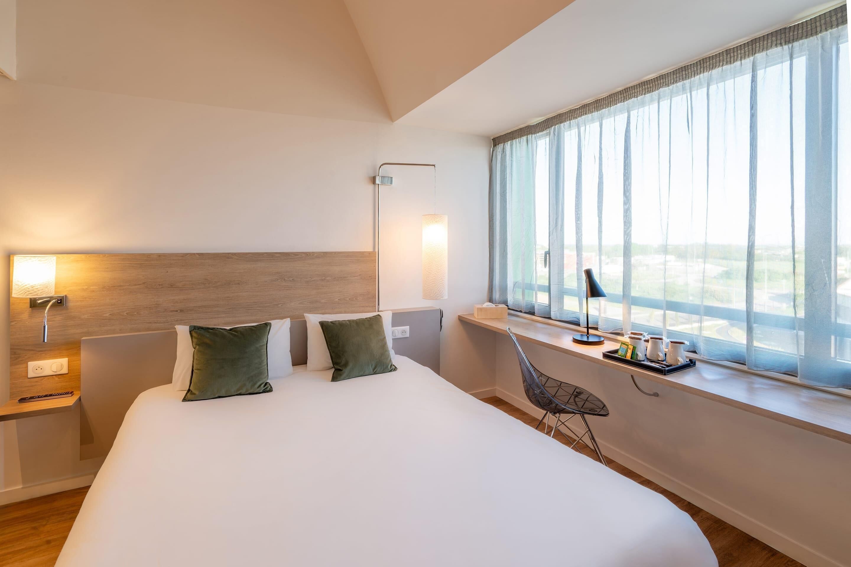Ein modernes Hotelzimmer mit einem großen Bett, Nachttischlampen, einem Schreibtisch und einem Fenster mit Blick.