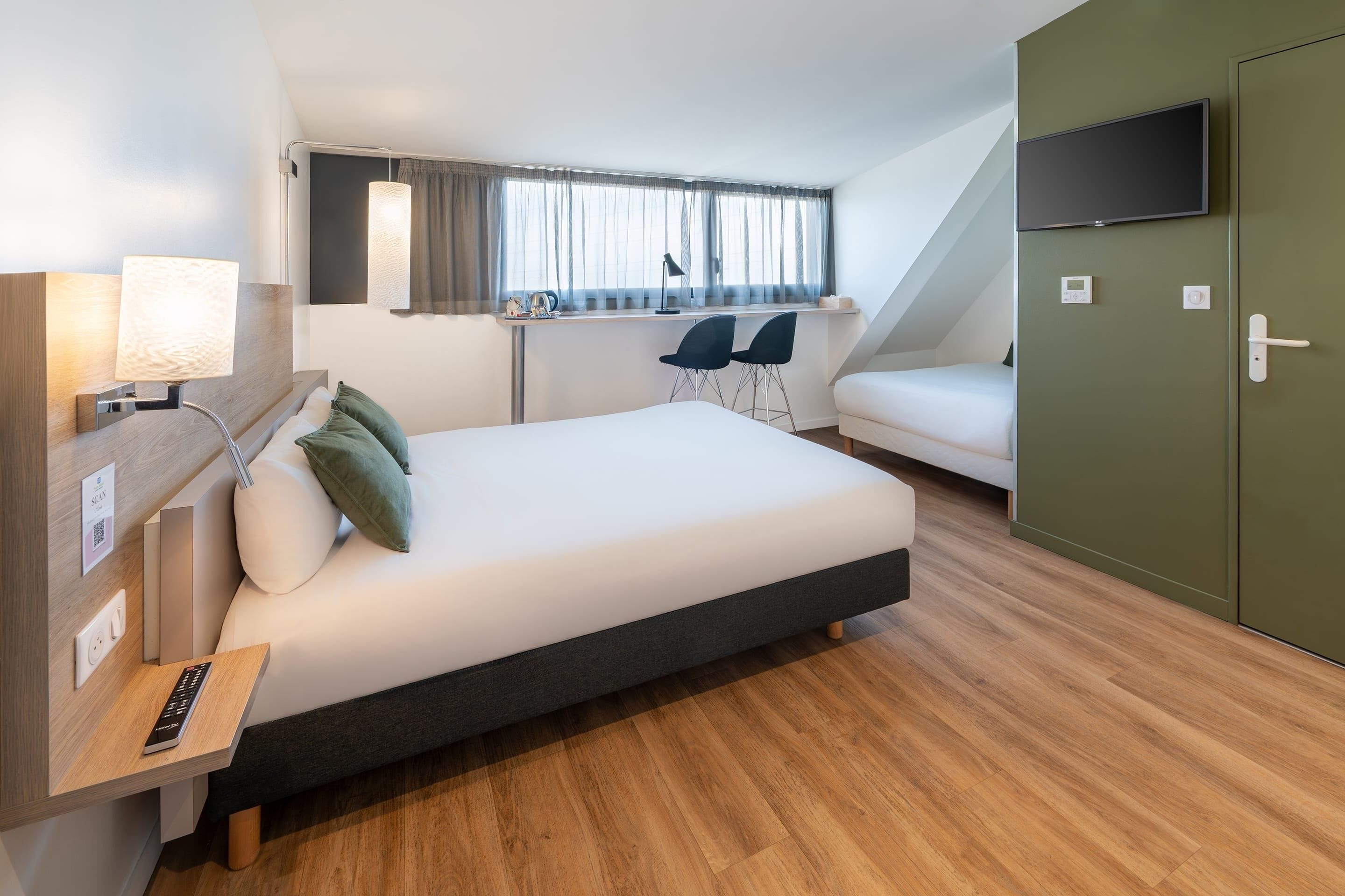 Une chambre d’hôtel moderne équipée d’un lit, d’une table de chevet, d’une lampe, d’une télévision et d’une fenêtre avec des rideaux.