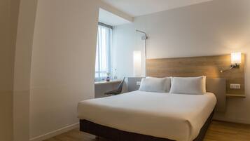 Een moderne hotelkamer met een groot bed, nachtkastje, lamp en een raam met gordijnen.