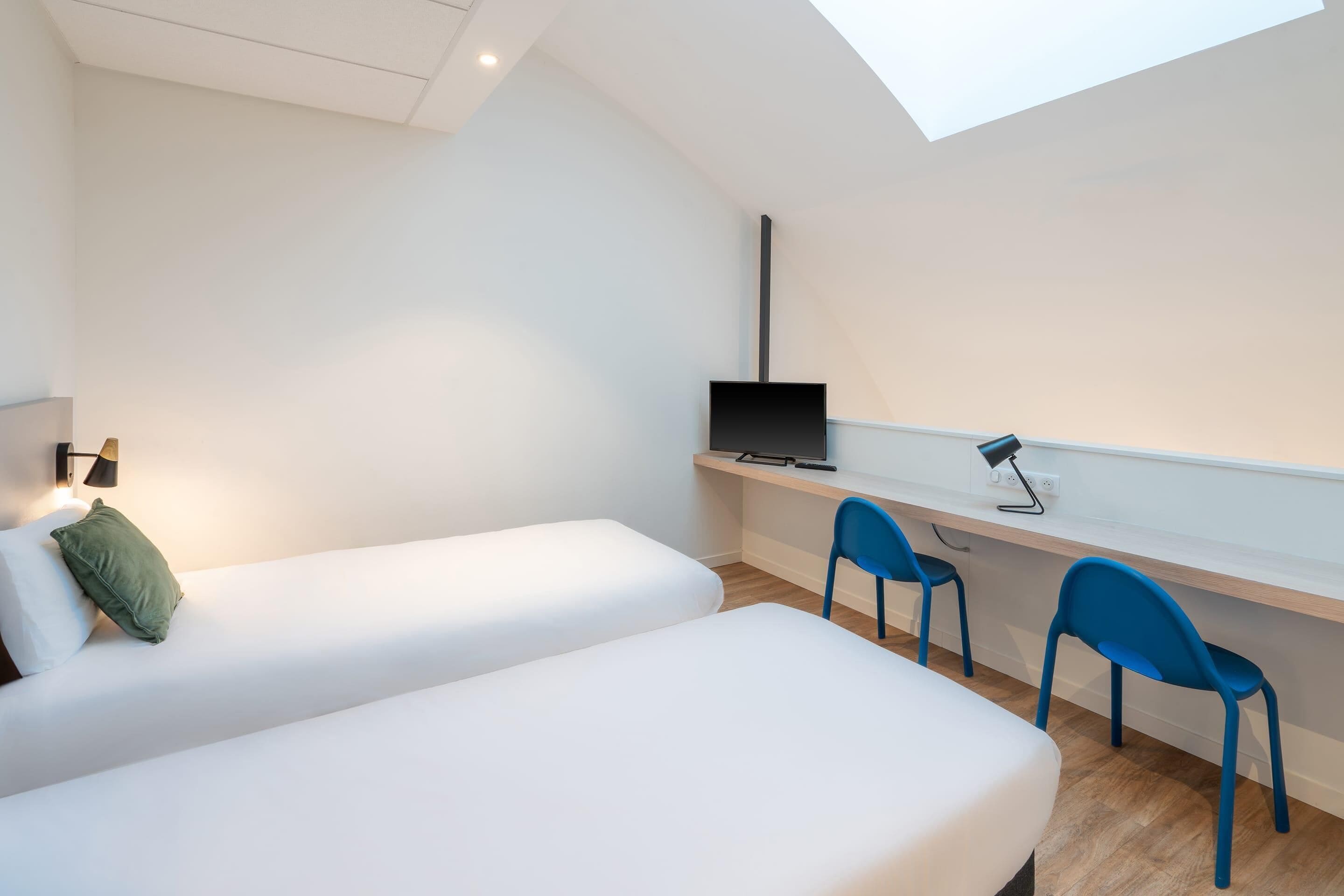 A bedroom with two beds, a desk with a computer, and a skylight.