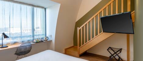 Un dormitorio con cama, un escritorio con silla, un televisor montado en la pared y una escalera.