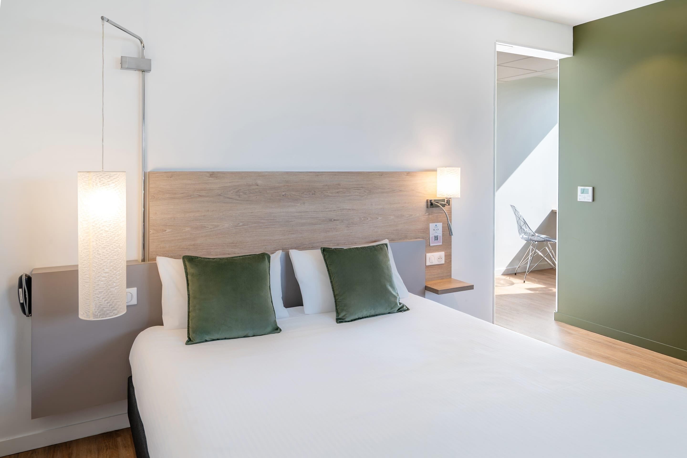 A hotel room with a large bed, a wooden headboard, a nightstand with a lamp, and a view of a balcony.
