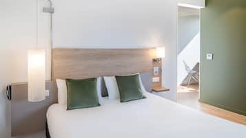 A hotel room with a large bed, a wooden headboard, a nightstand with a lamp, and a view of a balcony.
