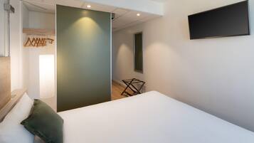 Een moderne hotelkamer met een bed, een kapstok, een tv aan de muur en een kleine tafel.
