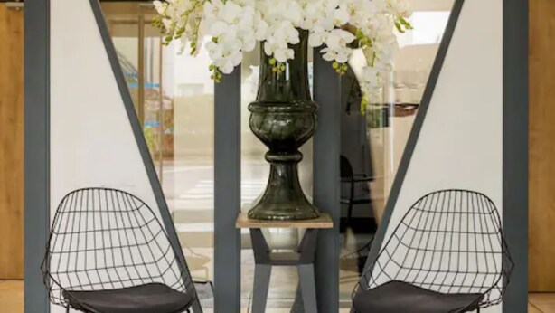Een modern interieur met een grote vaas witte bloemen op een voetstuk, twee open armstoelen en een glazen scheidingswand.