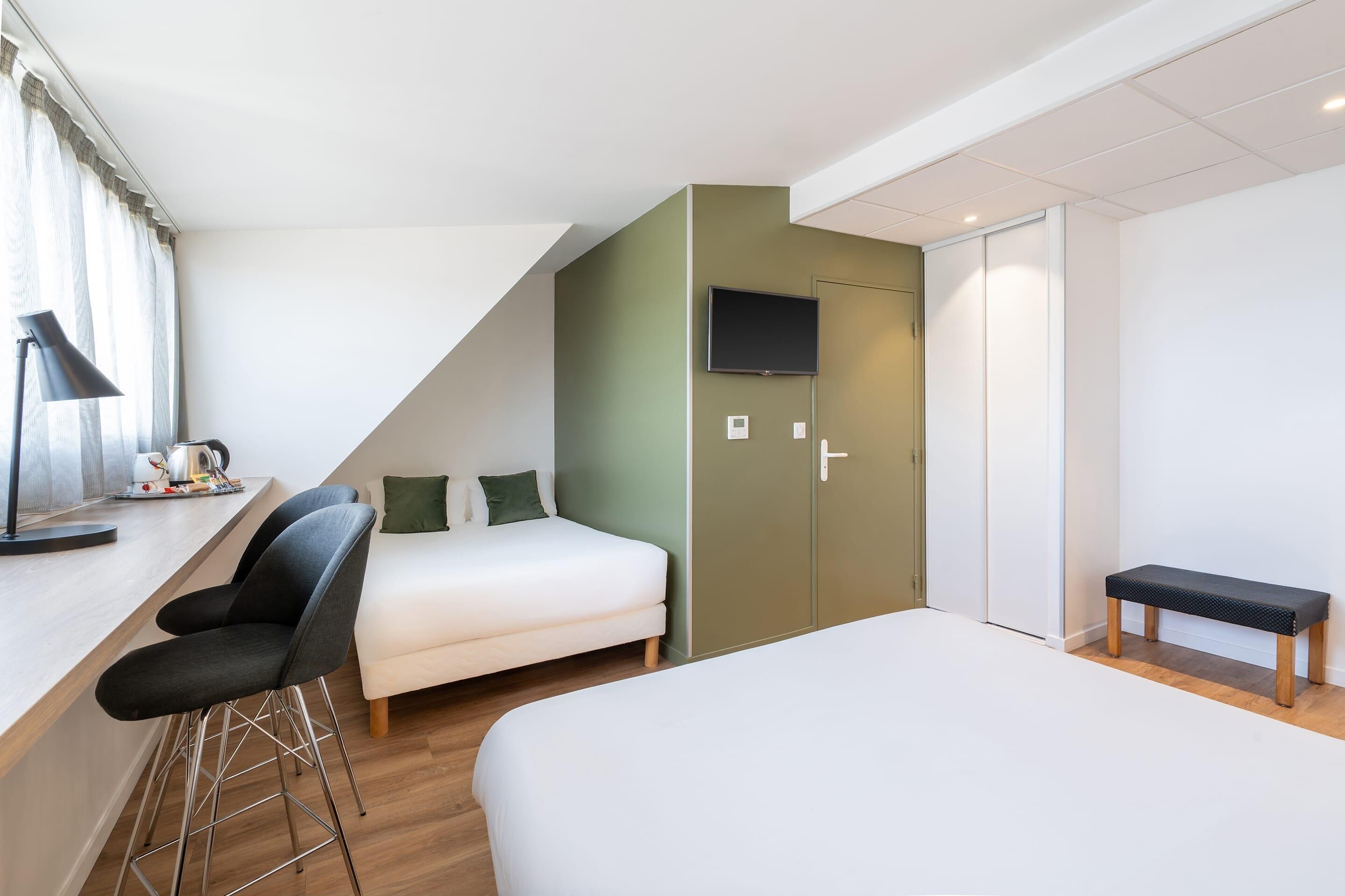 A modern hotel room with a bed, a desk with a chair, a TV mounted on the wall, and a bench.