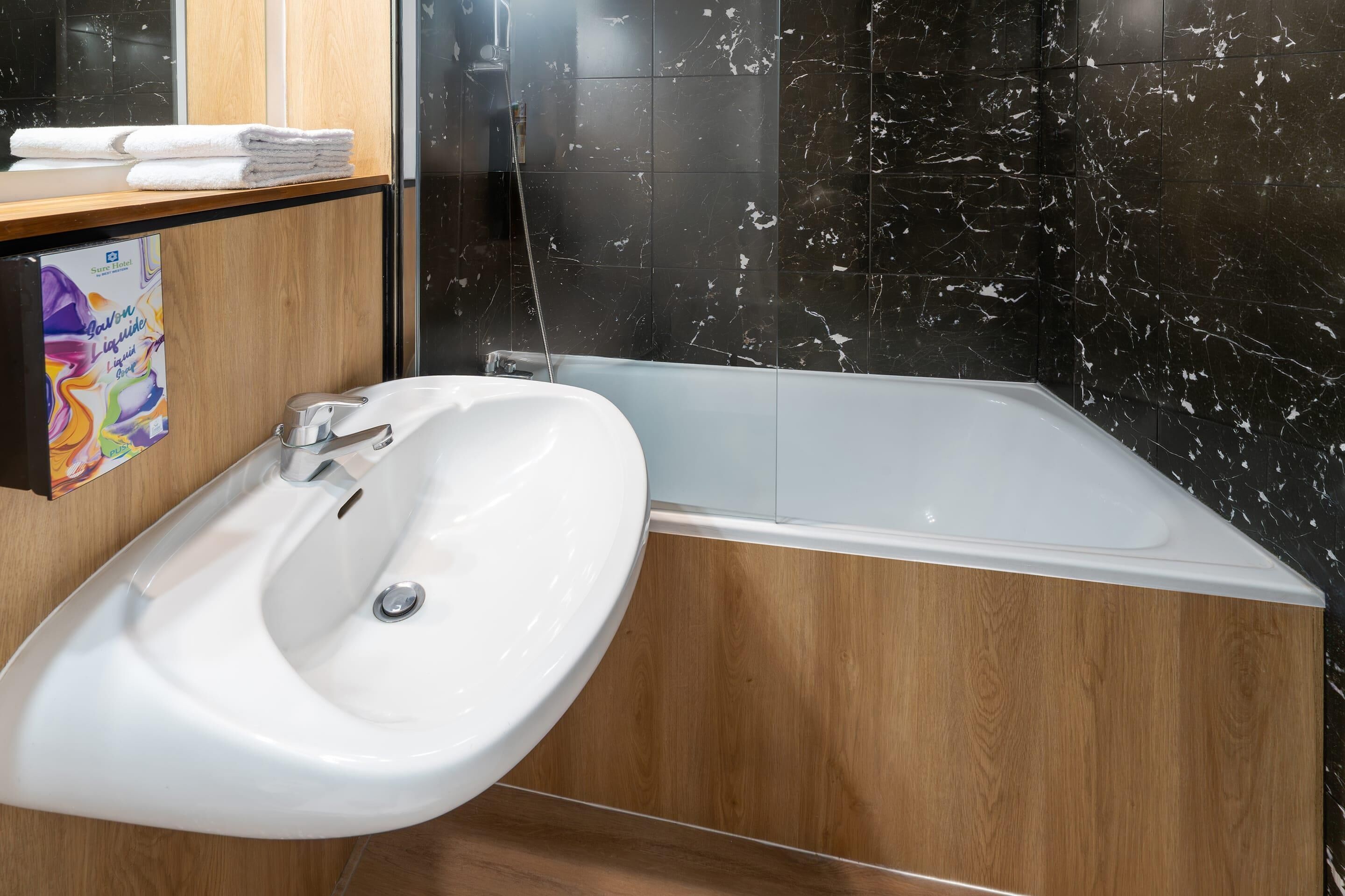 A bathroom with a white sink, a bathtub, and a wooden vanity.