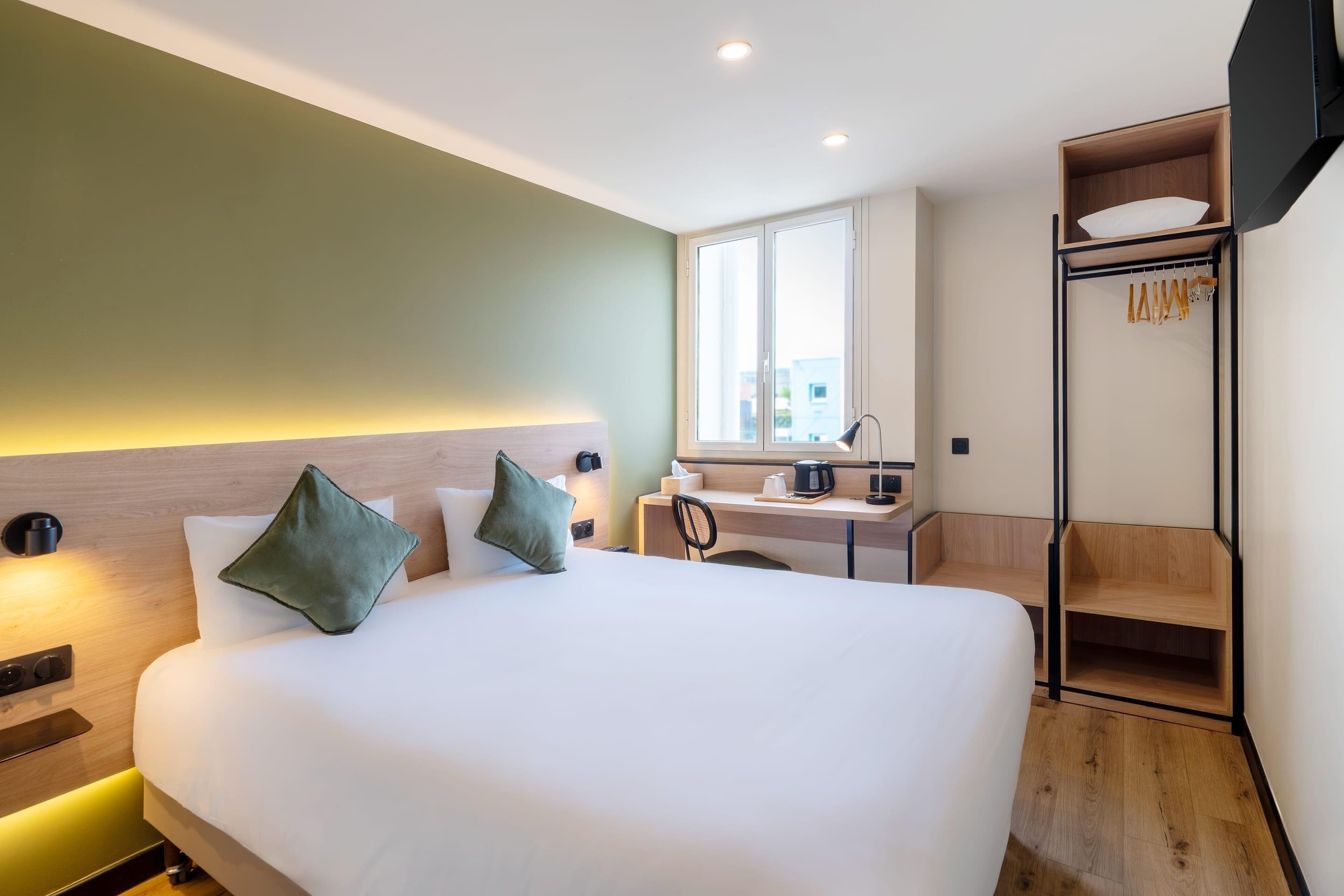 Una habitación de hotel con cama, escritorio, silla, estante y televisor.