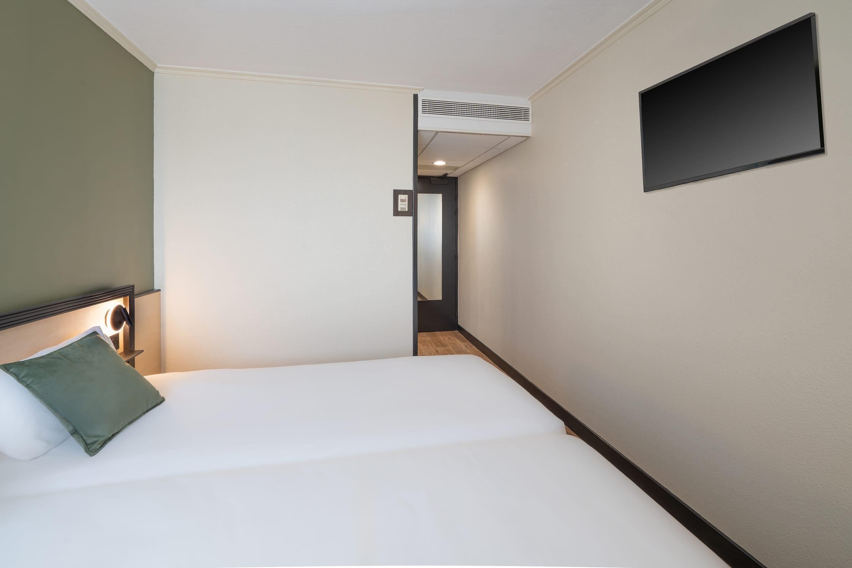 Een hotelkamer met een bed, een tv aan de muur en een gang naar een andere kamer.