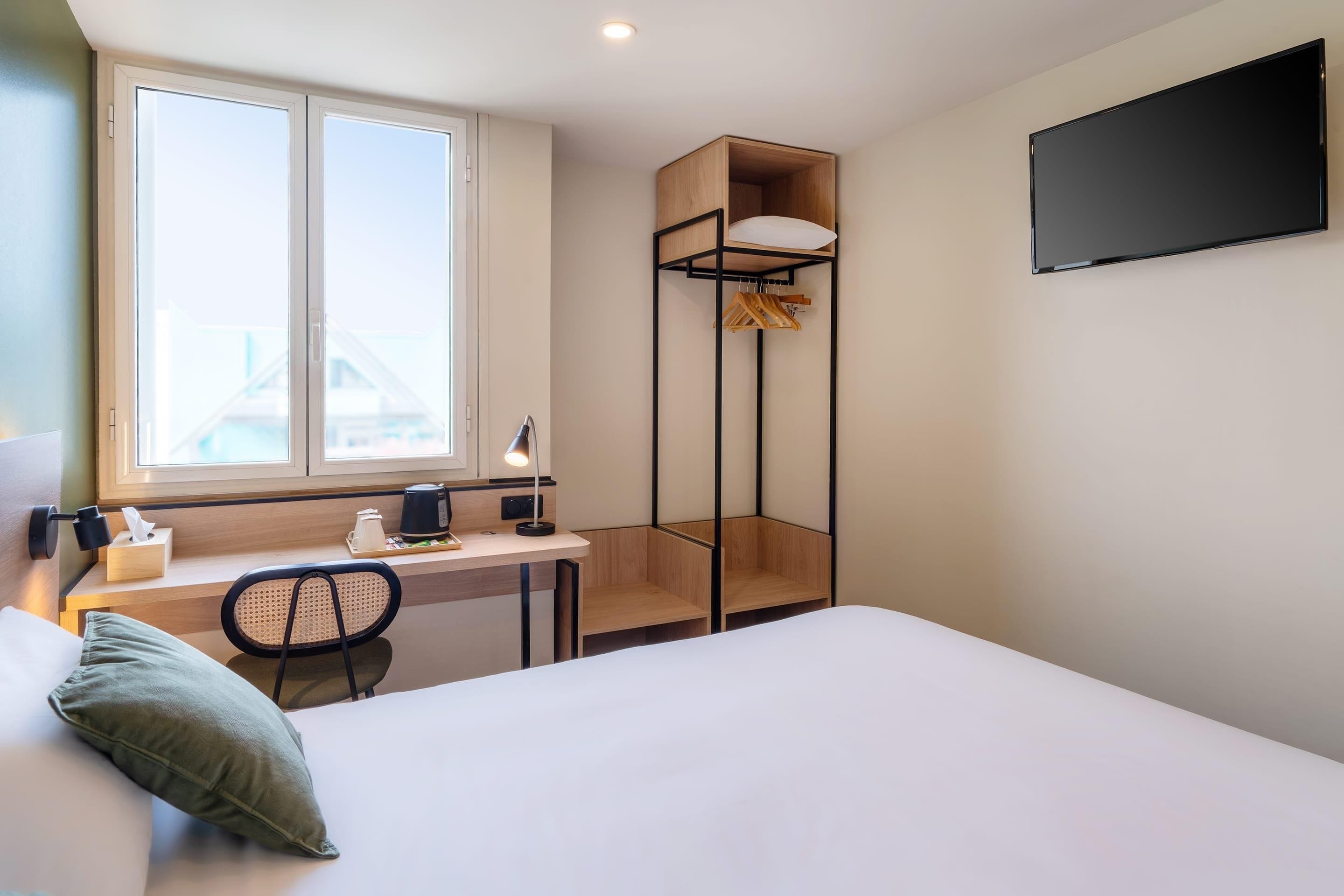 A hotel room with a bed, desk, chair, and a TV mounted on the wall.