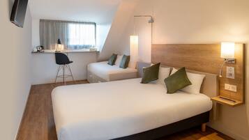 A hotel room with a large bed, a desk, a chair, and a TV.