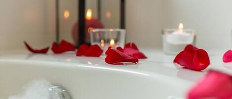 A bathtub with rose petals and candles, suggesting a romantic setting.