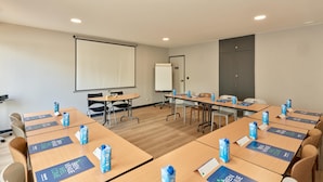 A conference room with tables, chairs, a projector screen, a whiteboard, and water bottles.