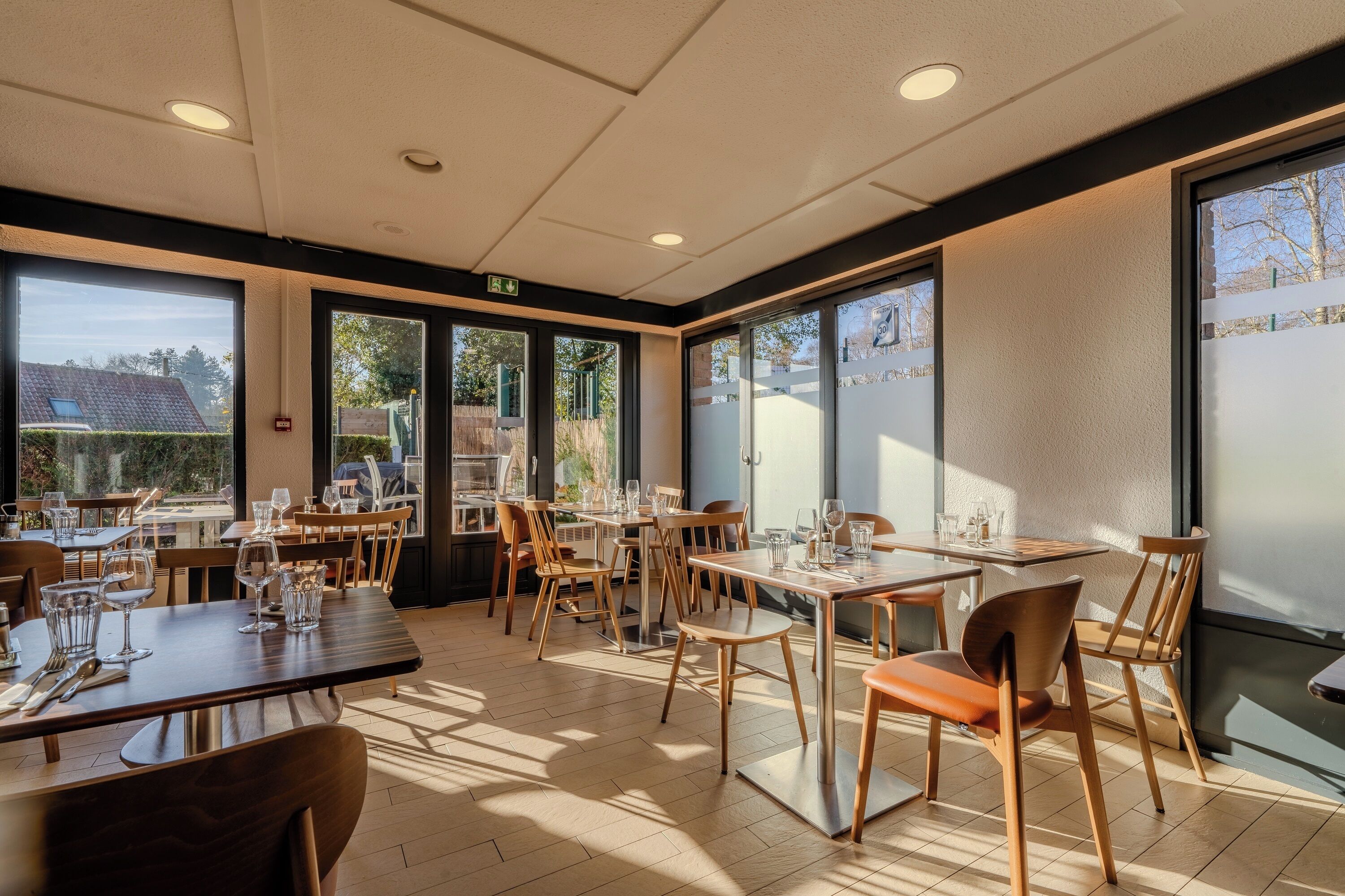 A restaurant with multiple tables and chairs, large windows, and a tiled floor.