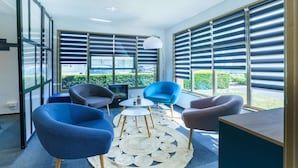 Una habitación moderna con ventanas amplias, un tapete redondo tejido y dos sillas azules.