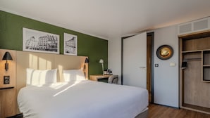Habitación de hotel con una cama grande, un escritorio, una silla, un armario y dos cuadros en la pared.