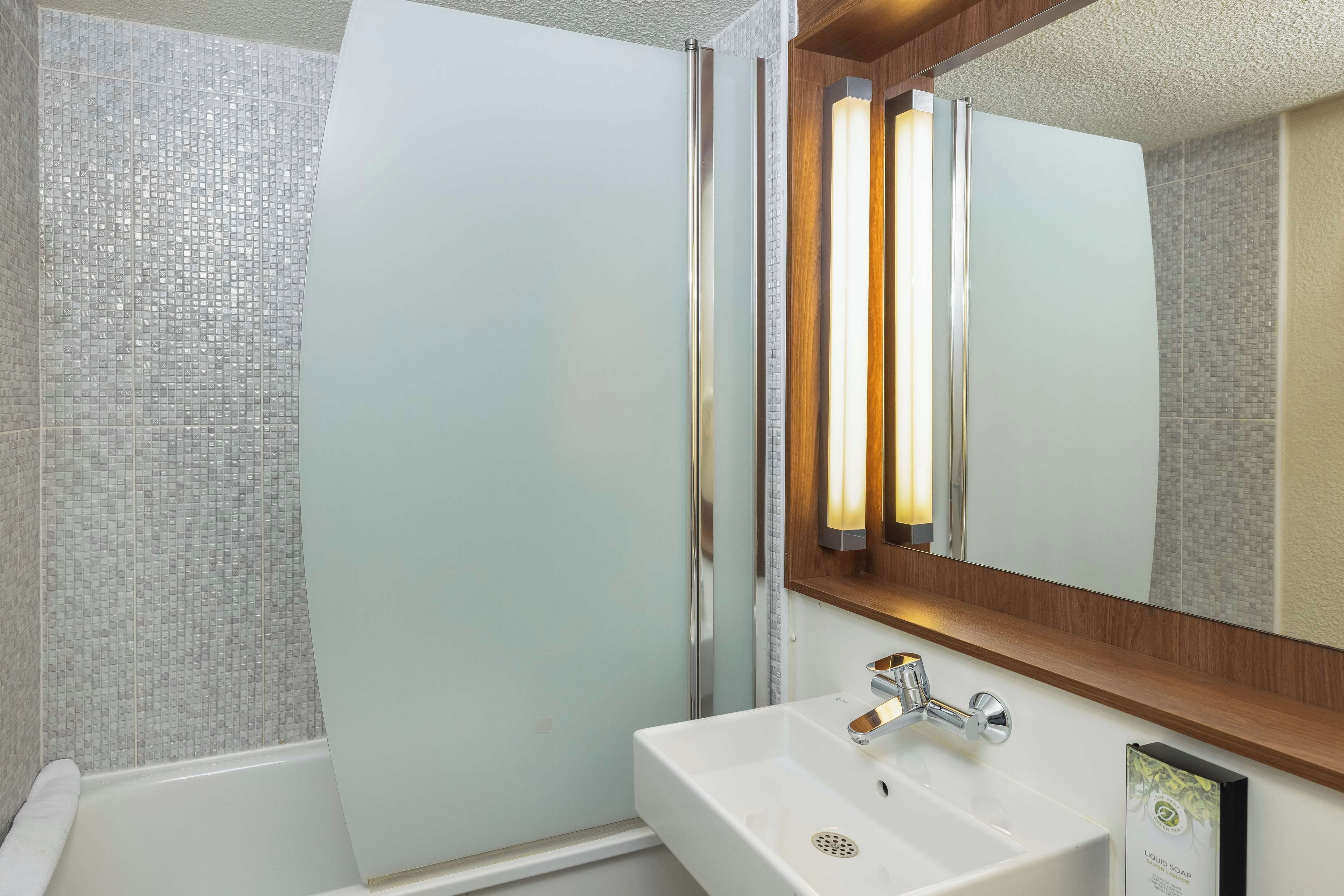 Un baño moderno con cabina de ducha de vidrio, un lavamanos blanco con grifo cromado y un espejo con marco de madera.