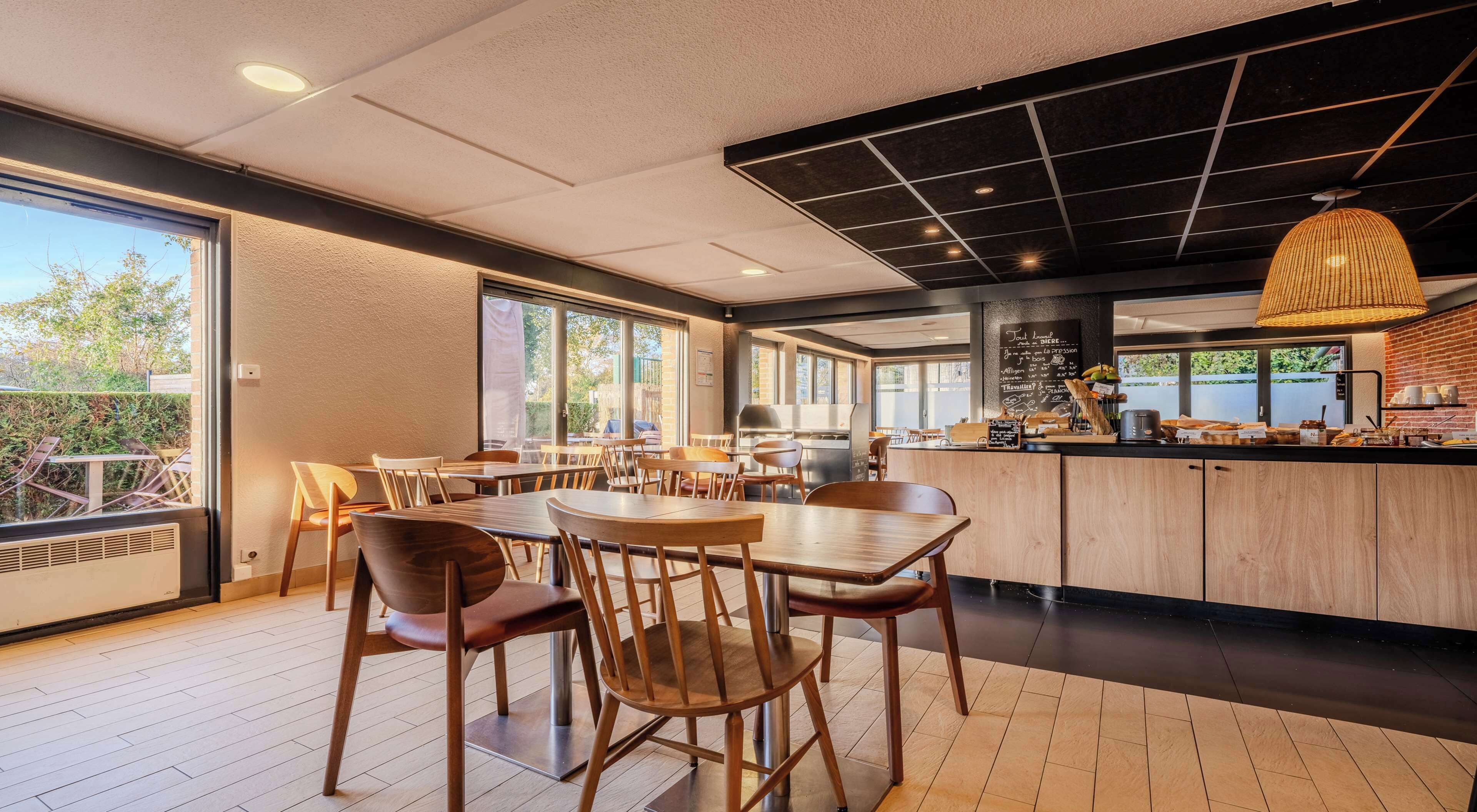 Ein modernes Café mit Holztischen und -stühlen, einer Theke mit Speisekarte und großen Fenstern mit Blick ins Freie.
