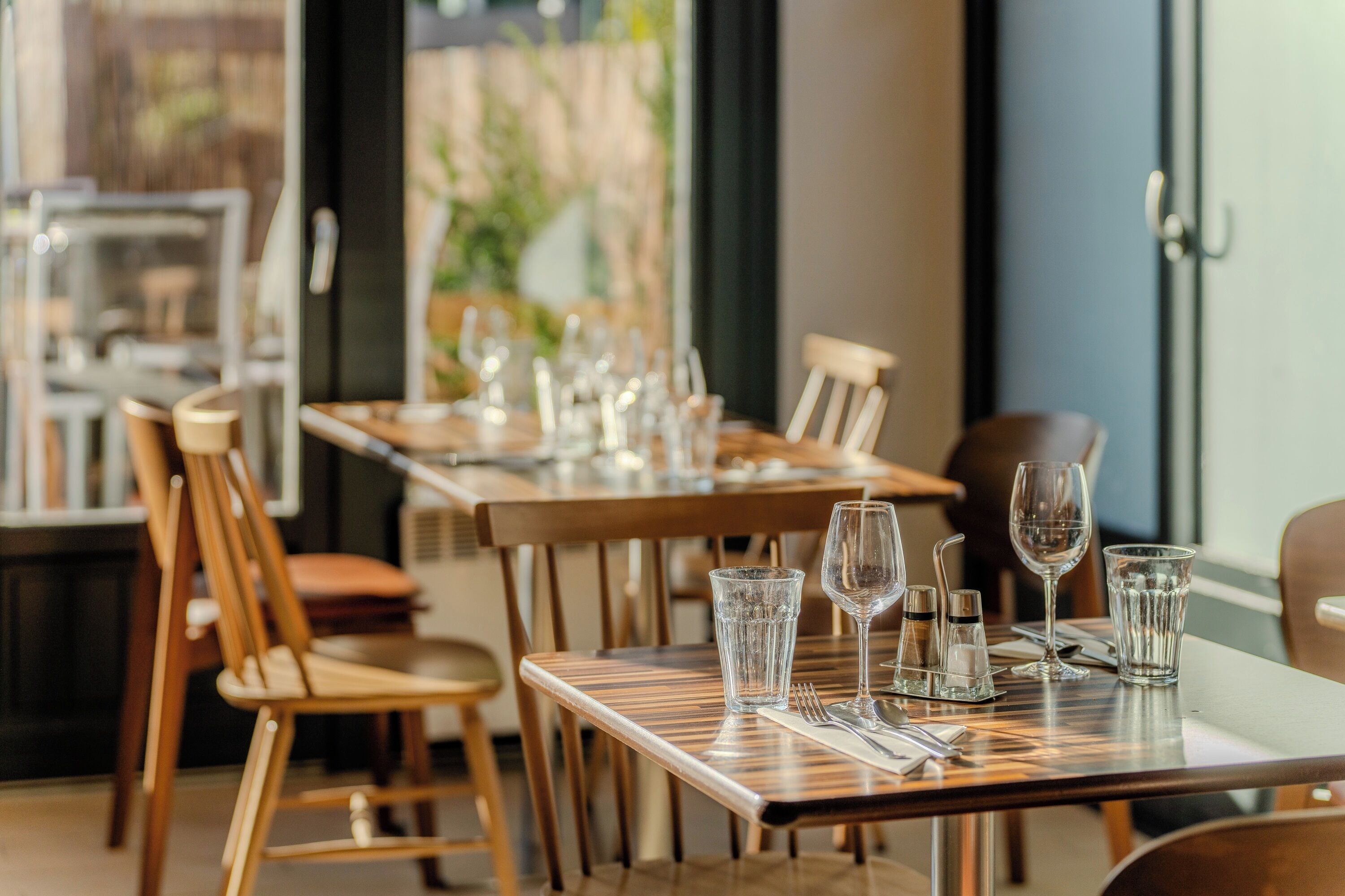 A restaurant with wooden tables and chairs, clear glasses, and cutlery.