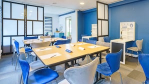 Un salón de conferencias con sillas azules, una mesa larga y una pantalla de proyector.