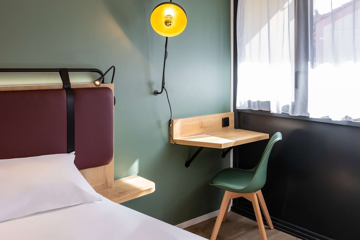 A hotel room with a bed, a desk, a chair, and a window with curtains.