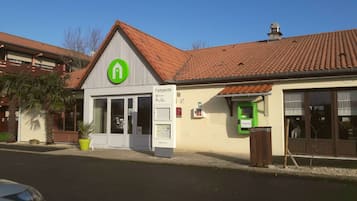 Un bâtiment avec un logo vert, une enseigne indiquant qu’il s’agit d’un hôtel-restaurant et un distributeur automatique de billets vert.