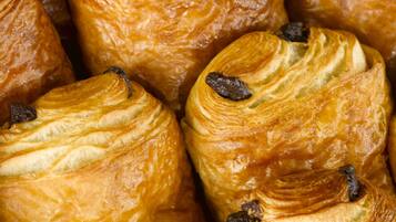 Une vue rapprochée de différentes sortes de viennoiseries, probablement des croissants, dont on distingue les couches et les raisins.