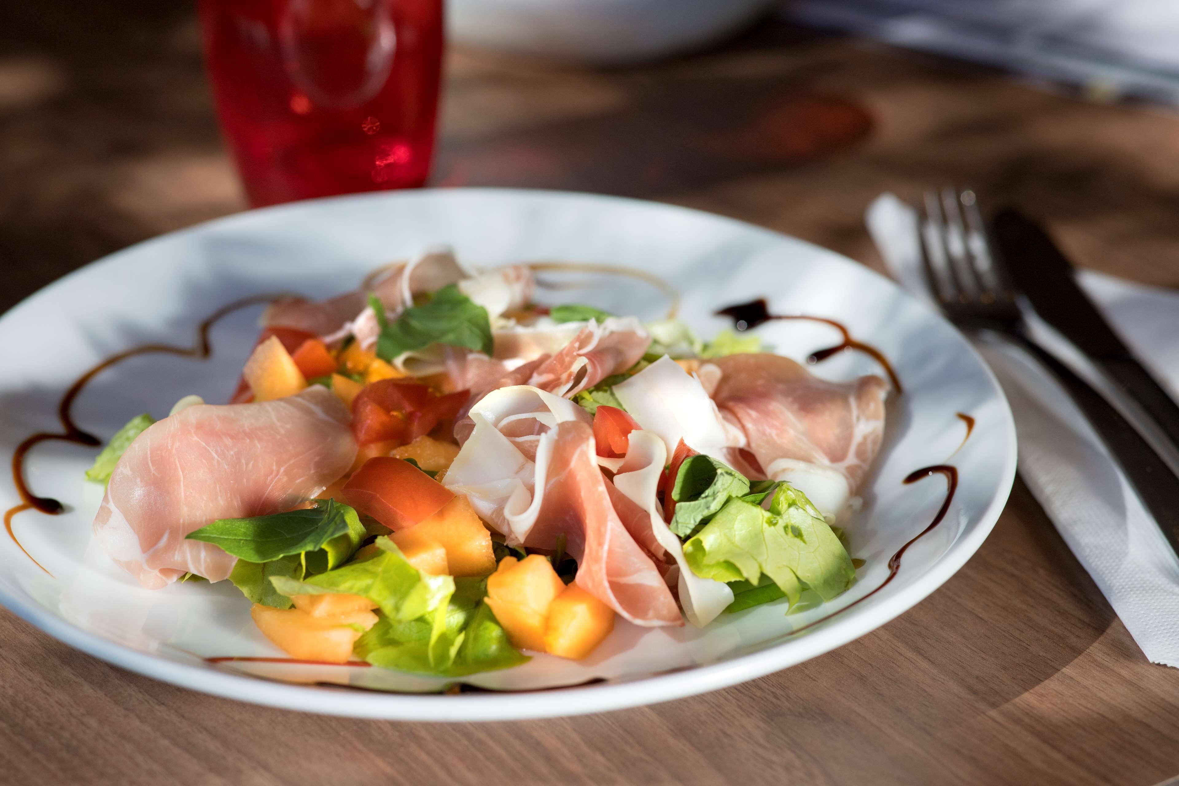 Une assiette de nourriture contenant divers ingrédients, notamment de la laitue, des tomates et un type de viande, présentée sur une assiette blanche à bord décoratif.