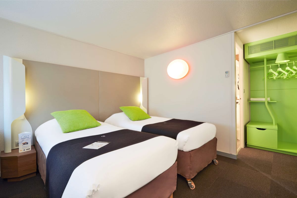 A hotel room with two beds, a green wall, a round light fixture, and a green wardrobe.