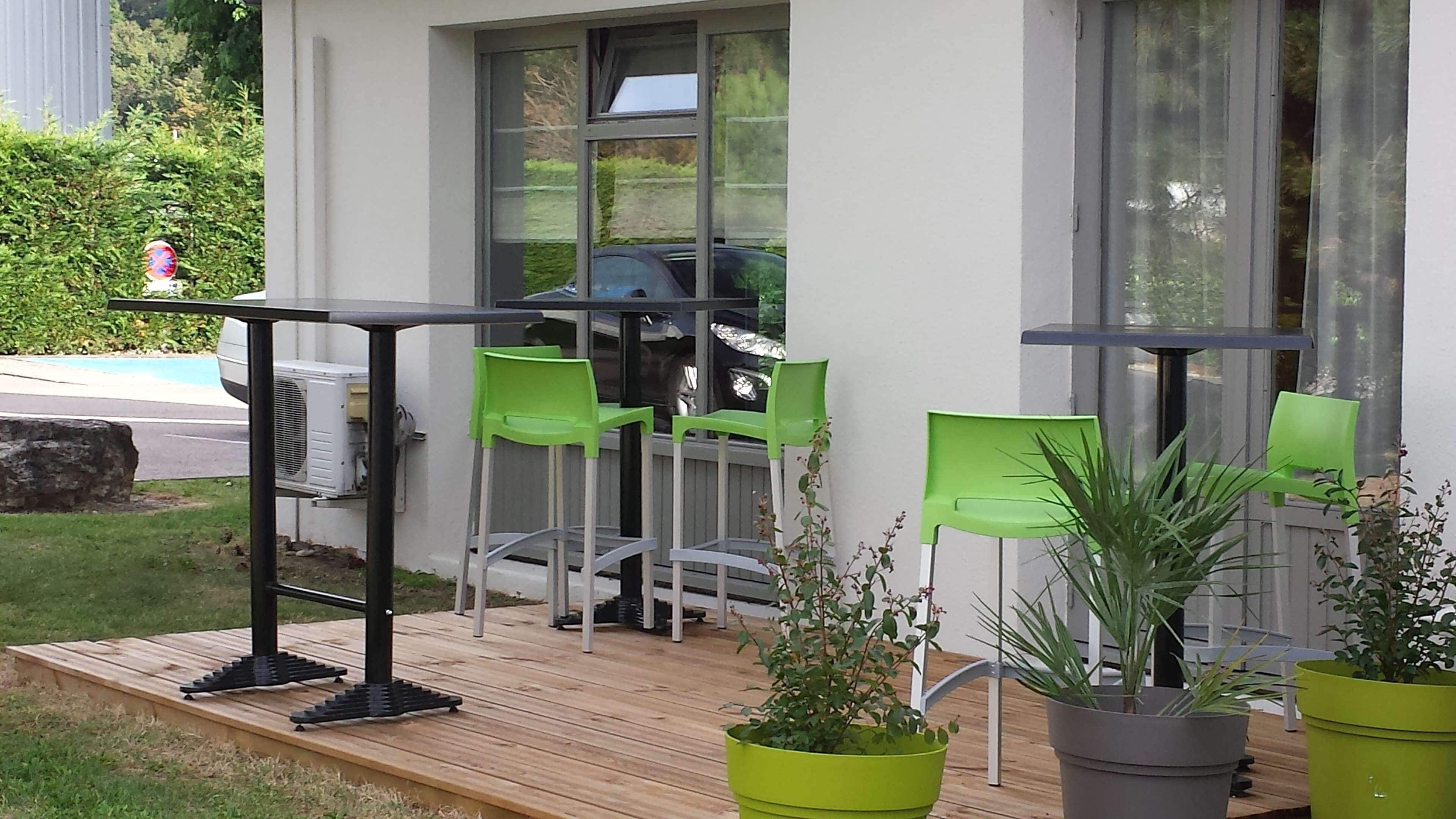 Une terrasse avec une plateforme en bois, des chaises vertes, une table et des plantes en pot.