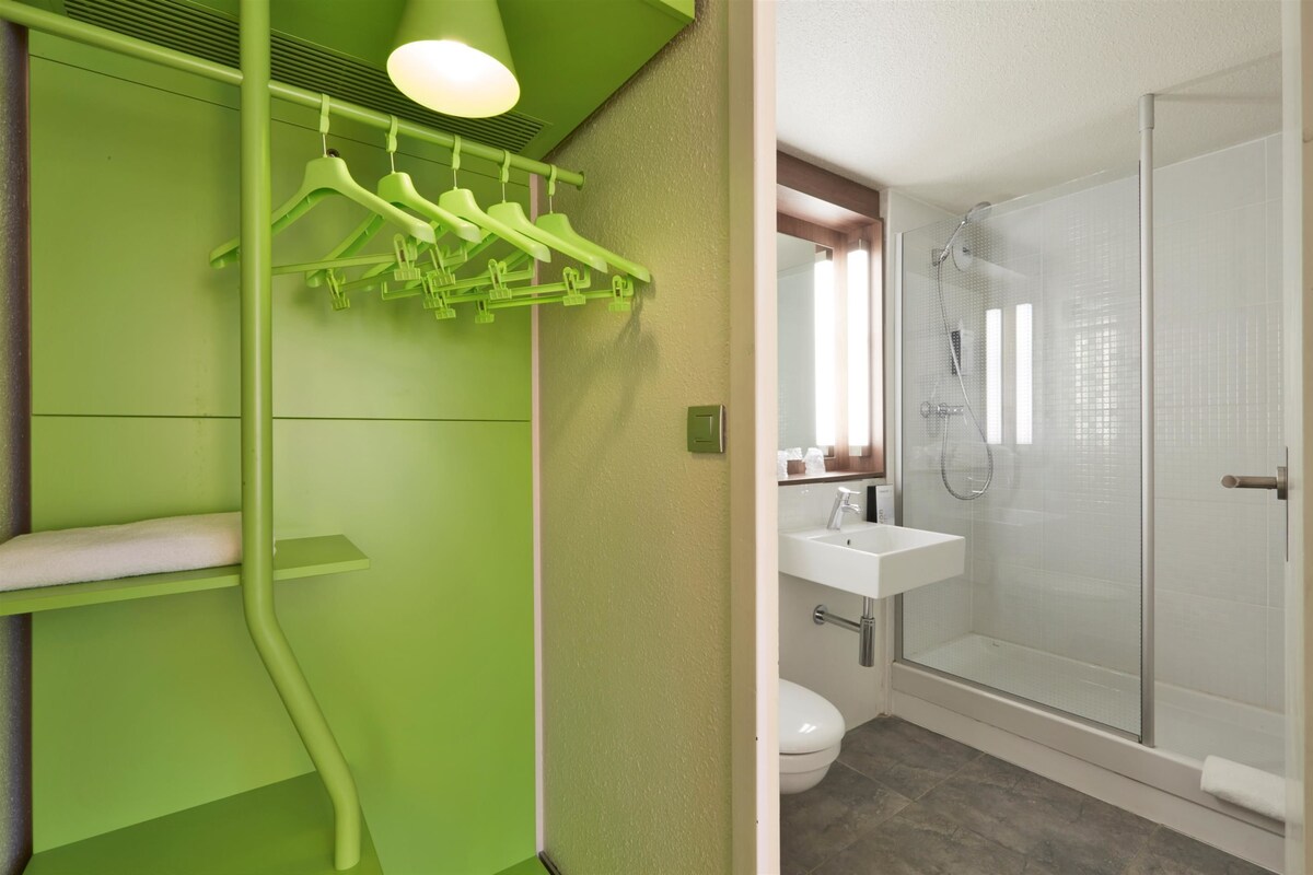 A bathroom with a green wall, a white sink, and a glass shower enclosure.