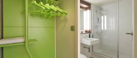 A bathroom with a green wall, a white sink, and a glass shower enclosure.