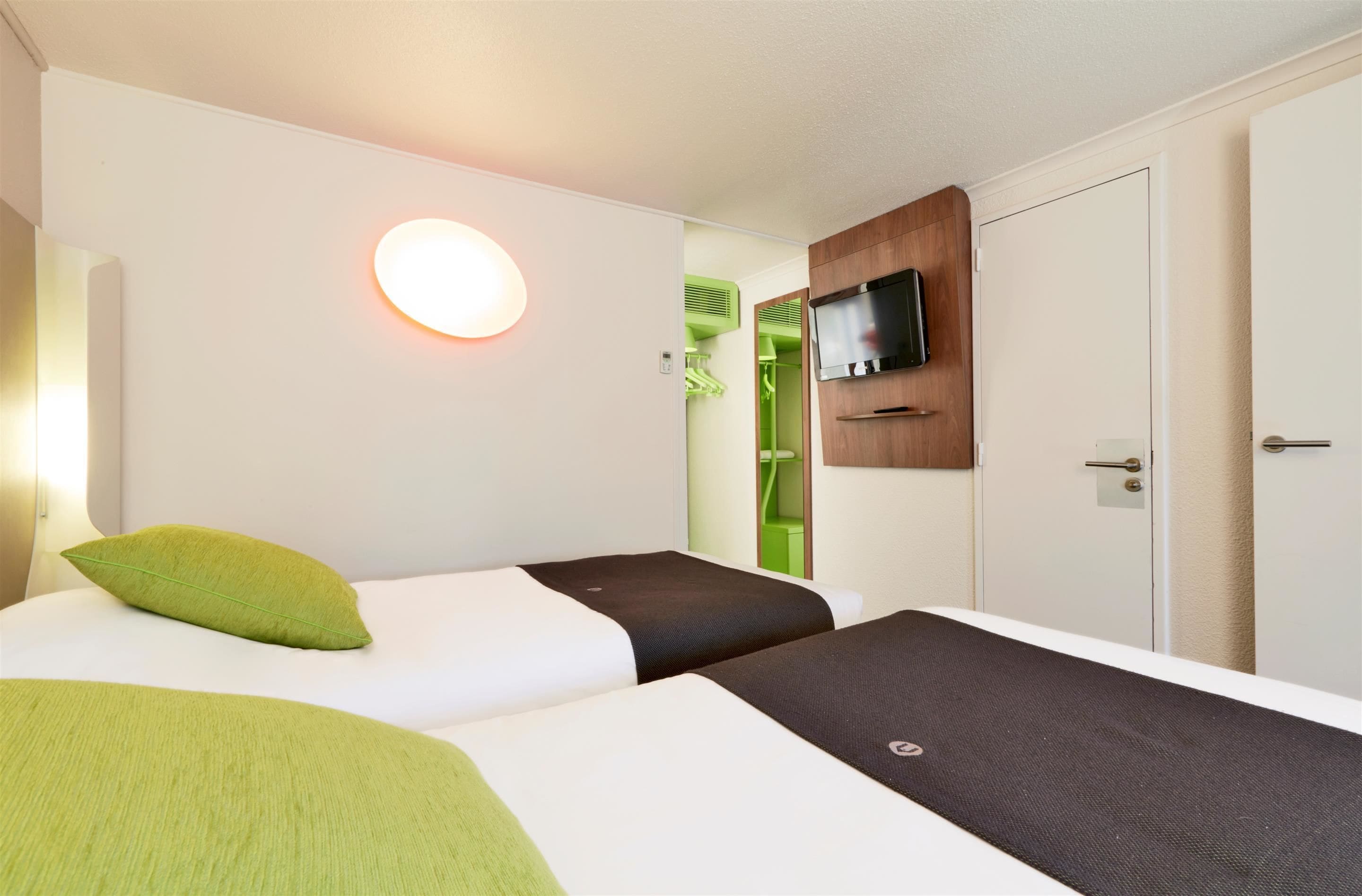 Une chambre d’hôtel avec deux lits, un téléviseur fixé au mur et une porte donnant sur la salle de bain.